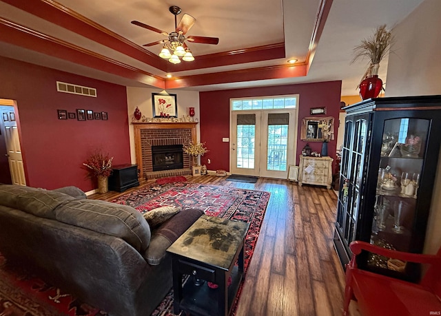 living area with visible vents, ceiling fan, a tray ceiling, a fireplace, and wood finished floors