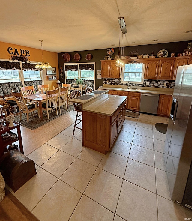 kitchen featuring brown cabinetry, a sink, stainless steel appliances, light countertops, and tasteful backsplash