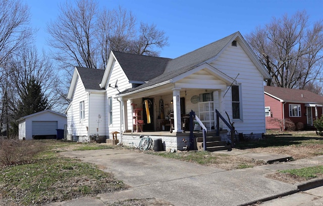 bungalow-style home with concrete driveway, roof with shingles, covered porch, a garage, and an outbuilding