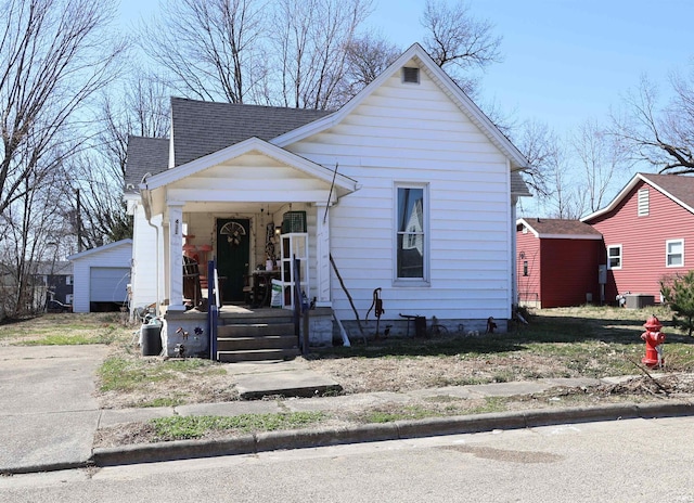 bungalow-style home with covered porch, a shingled roof, an outdoor structure, concrete driveway, and central air condition unit