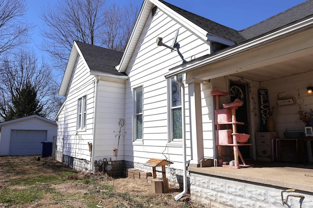 view of side of home featuring an outbuilding, driveway, a garage, and roof with shingles