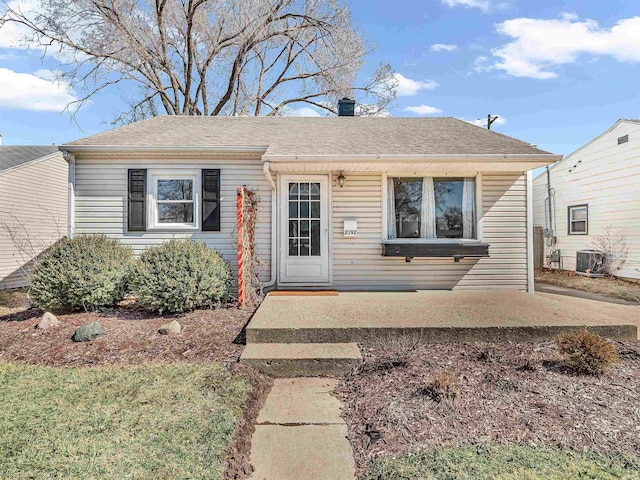 bungalow-style home featuring central AC unit and roof with shingles