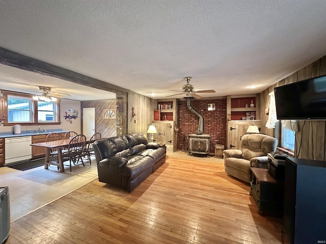 living room featuring a wood stove, light wood-style flooring, wood walls, and a textured ceiling