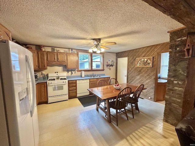 kitchen featuring a sink, white appliances, wood walls, brown cabinetry, and light floors