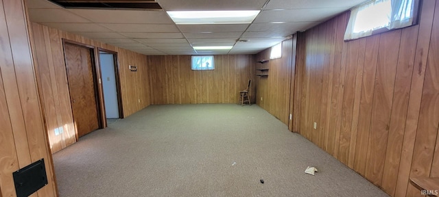 below grade area with wooden walls, light colored carpet, and a drop ceiling