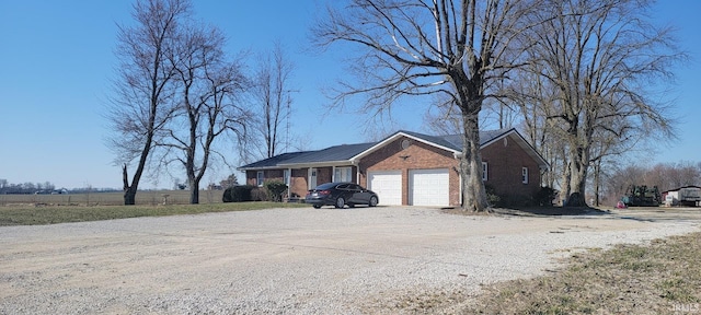 ranch-style house featuring gravel driveway, an attached garage, and brick siding