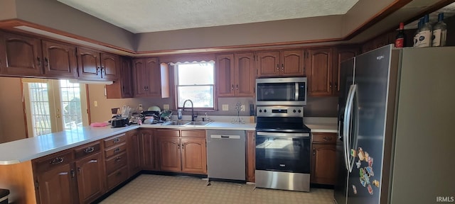 kitchen with a sink, appliances with stainless steel finishes, a peninsula, and light countertops