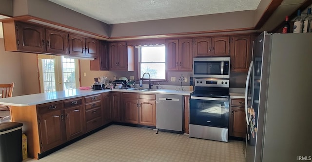 kitchen featuring light floors, a peninsula, a sink, stainless steel appliances, and light countertops