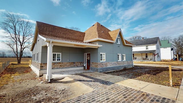 back of house with stucco siding, brick siding, and a shingled roof