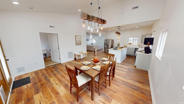 dining area featuring light wood finished floors, visible vents, and high vaulted ceiling