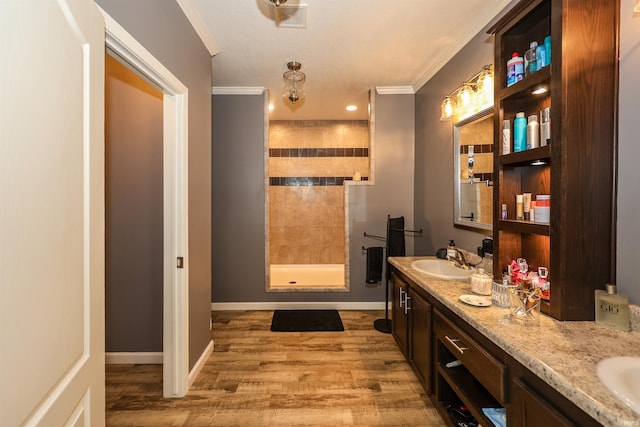 bathroom with ornamental molding, a sink, wood finished floors, a tile shower, and double vanity