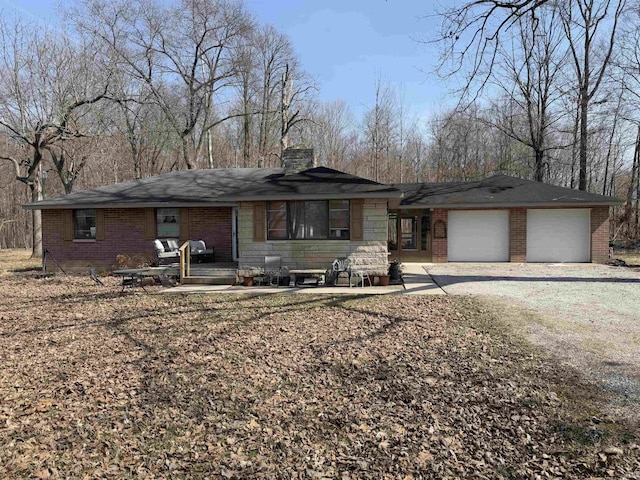 view of front of house with brick siding, an attached garage, a chimney, and driveway