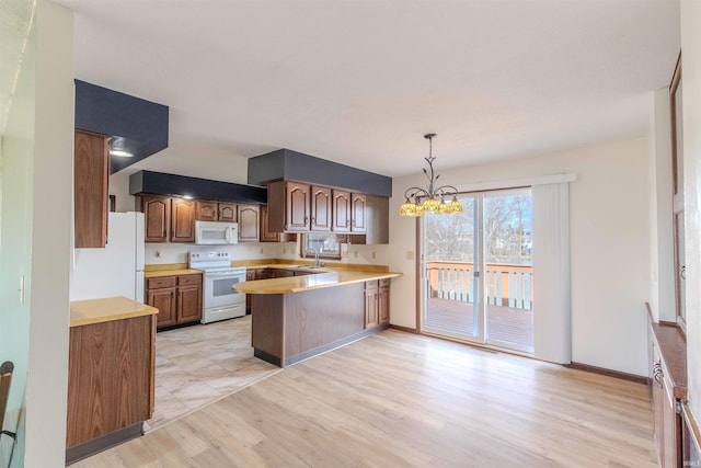 kitchen with white appliances, light wood-style floors, a peninsula, light countertops, and a chandelier