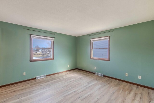 empty room featuring wood finished floors, visible vents, and baseboards