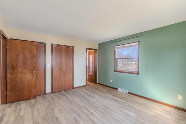 unfurnished bedroom featuring baseboards, visible vents, two closets, and light wood-type flooring