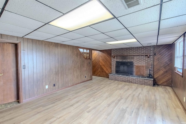 unfurnished living room with visible vents, a brick fireplace, wood finished floors, and wood walls