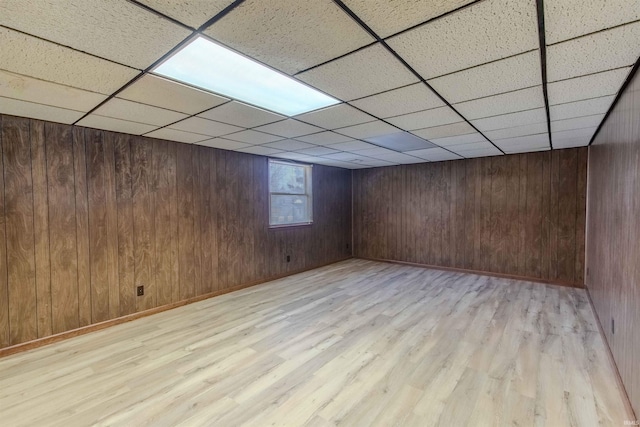 below grade area featuring a drop ceiling, wood walls, baseboards, and light wood-style floors