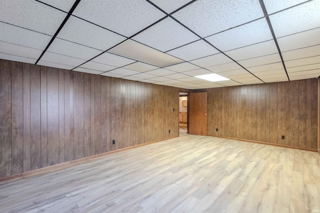 finished below grade area with wooden walls, a drop ceiling, baseboards, and wood finished floors