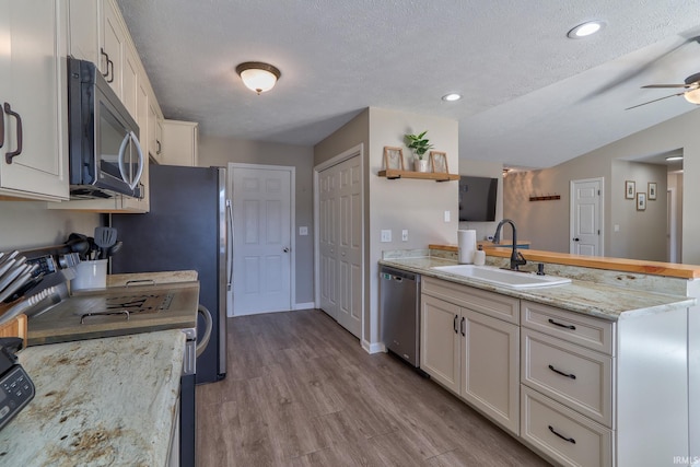 kitchen with appliances with stainless steel finishes, a peninsula, wood finished floors, white cabinetry, and a sink