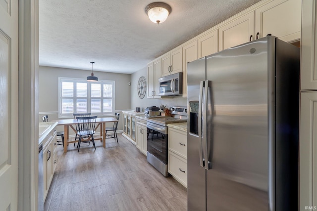 kitchen with pendant lighting, light countertops, appliances with stainless steel finishes, light wood-style floors, and a textured ceiling