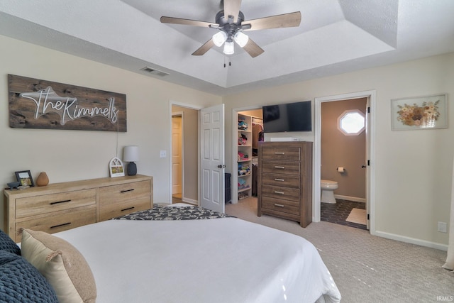 bedroom with baseboards, a walk in closet, a raised ceiling, and light carpet