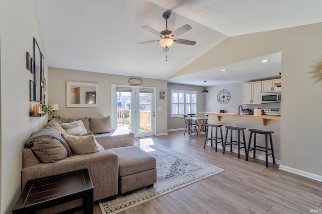 living area featuring light wood finished floors, a ceiling fan, baseboards, and vaulted ceiling