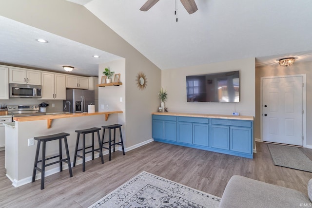 kitchen featuring light wood-style flooring, appliances with stainless steel finishes, a breakfast bar, and vaulted ceiling