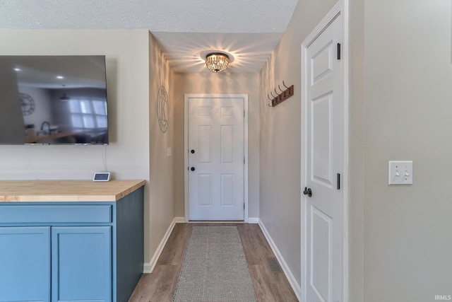 doorway to outside featuring wood finished floors, baseboards, and a textured ceiling