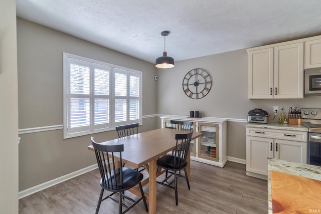 dining area with light wood-type flooring, baseboards, and a textured ceiling