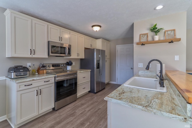 kitchen with a sink, light wood-type flooring, light countertops, stainless steel appliances, and open shelves