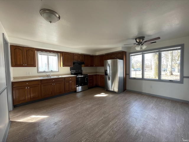 kitchen featuring under cabinet range hood, light countertops, appliances with stainless steel finishes, wood finished floors, and a sink