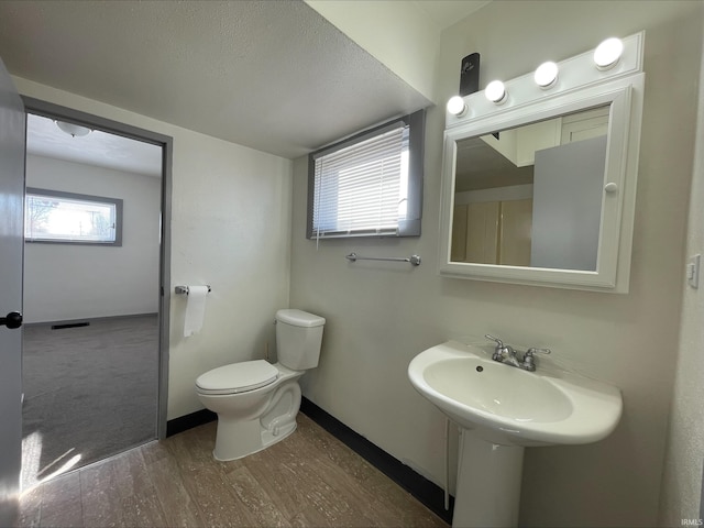 half bath featuring visible vents, toilet, wood finished floors, and baseboards