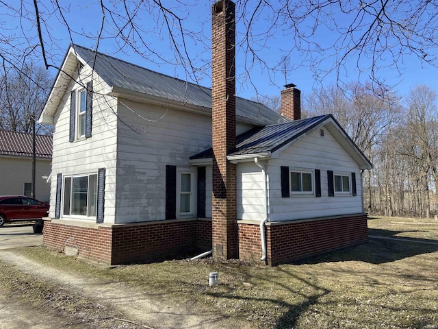 view of property exterior with a chimney, brick siding, and metal roof