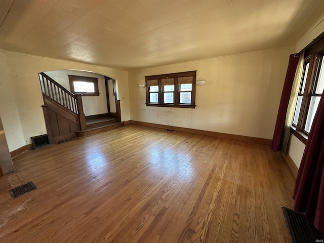 unfurnished living room featuring visible vents, baseboards, arched walkways, stairs, and wood-type flooring