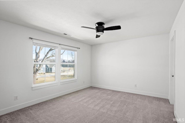 spare room with visible vents, ceiling fan, baseboards, light carpet, and a textured ceiling