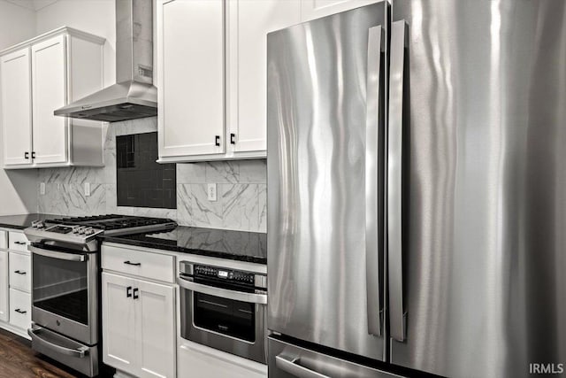 kitchen with backsplash, dark stone countertops, stainless steel appliances, white cabinetry, and wall chimney exhaust hood