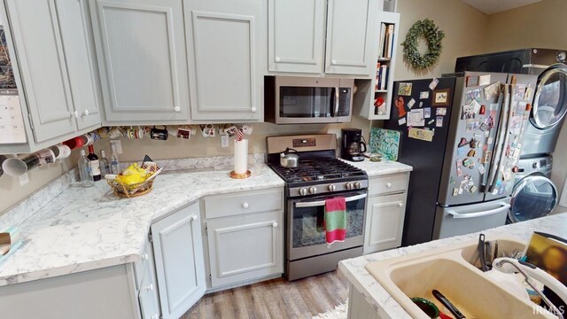 kitchen featuring light wood-style flooring, stacked washer and clothes dryer, white cabinets, stainless steel appliances, and a sink