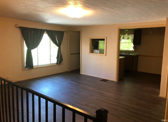 unfurnished room featuring a textured ceiling, visible vents, dark wood-style flooring, and a sink