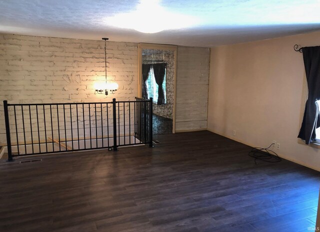 unfurnished room with visible vents, brick wall, and wood finished floors