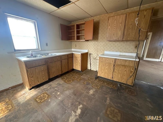 kitchen with brown cabinets, a sink, a drop ceiling, open shelves, and light countertops