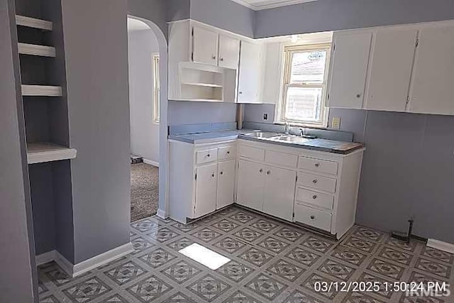 kitchen featuring open shelves, arched walkways, white cabinets, and a sink