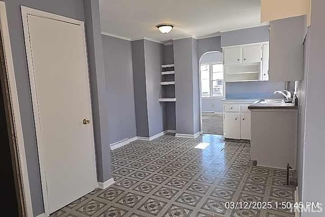 kitchen featuring open shelves, a sink, white cabinets, light countertops, and baseboards