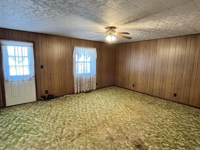 carpeted empty room featuring a ceiling fan and wood walls