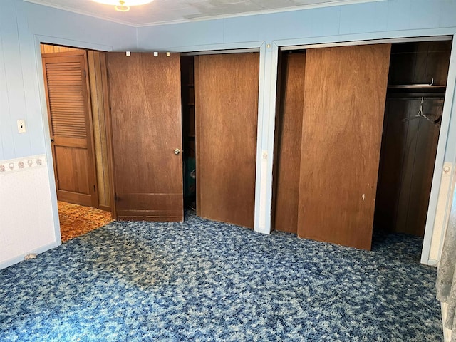 unfurnished bedroom with two closets, crown molding, and carpet floors