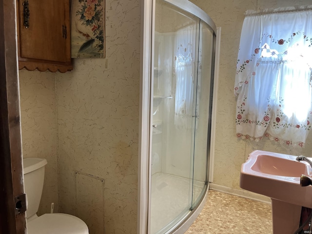 bathroom with wallpapered walls, a shower stall, and toilet