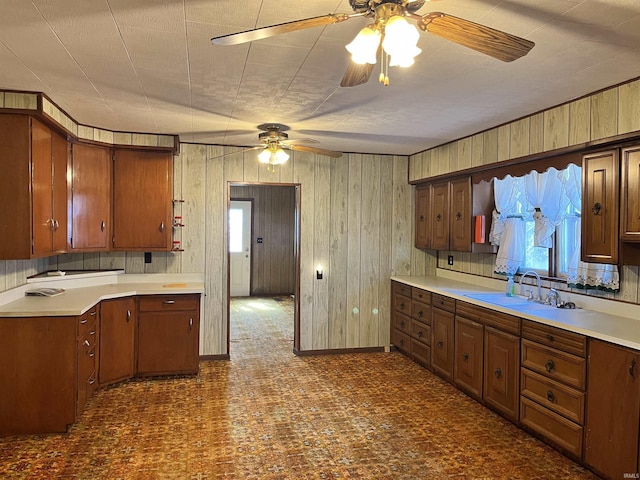 kitchen featuring ceiling fan, light countertops, wood walls, and a sink