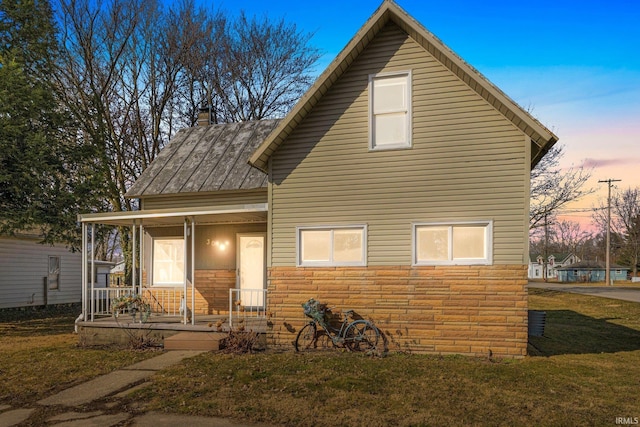 view of front of house with stone siding, a lawn, a porch, and a chimney