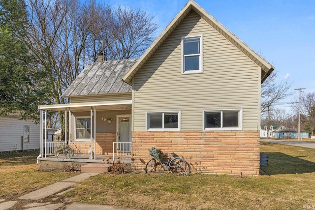 view of front facade featuring a front lawn, stone siding, a porch, metal roof, and a chimney