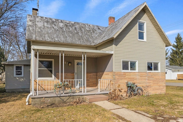 view of front facade featuring covered porch, a chimney, a front lawn, stone siding, and metal roof