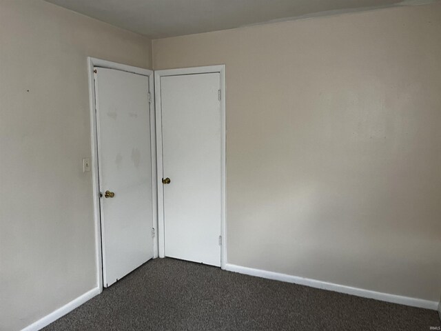 spare room featuring baseboards and dark carpet